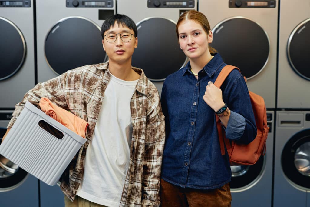 portrait two customers standing against washing machines public laundromat